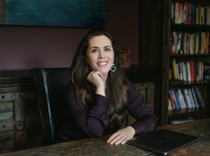 Dr. Claire Zammit smiling at her desk in front of a bookshelf