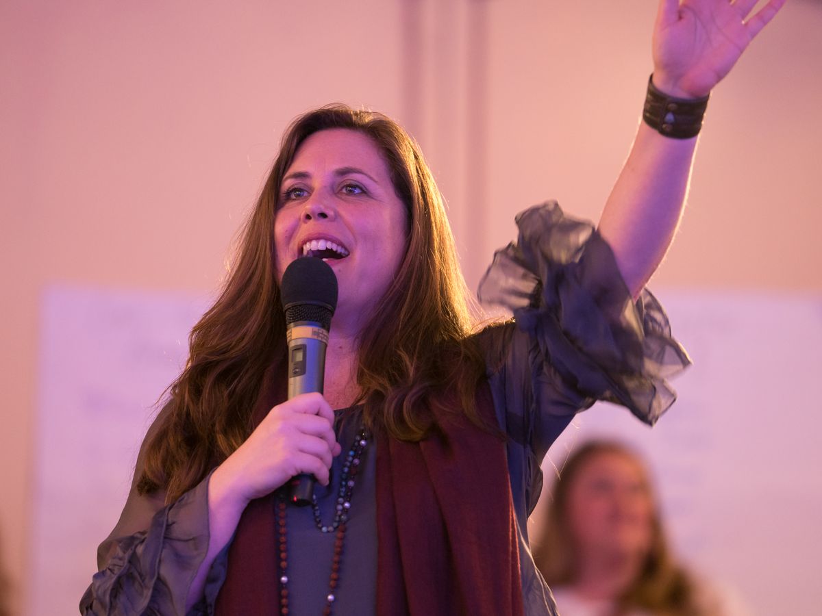 Dr. Claire Zammit speaking to a room of women, microphone in hand and arm raised